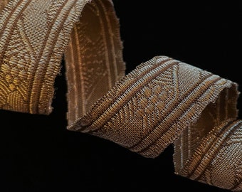 May include: A brown and white woven ribbon with a geometric pattern. The ribbon is curled and twisted.