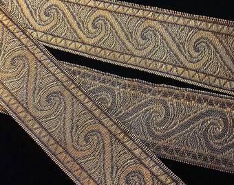 May include: Two pieces of gold trim with a repeating pattern of stylized waves. The trim is woven with a dark brown thread.