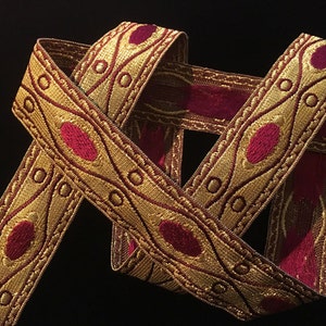 Puede incluir: Borde dorado y burdeos con un patrón repetido de círculos y óvalos. El borde tiene una textura en relieve y está tejido con un hilo metálico.