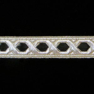 May include: A silver ribbon with a repeating geometric pattern of open diamond shapes. The ribbon has a metallic sheen and is likely used for decorative purposes in crafts or sewing projects. The background is black.