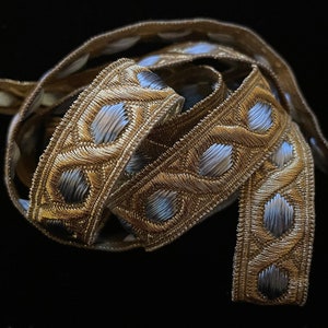 May include: Gold and silver trim with a geometric pattern. The trim is woven and has a raised design.