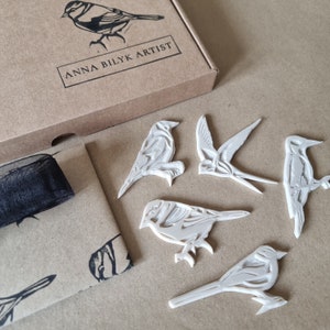 Five hand carved bird rubber lino stamps for hand printing including Woodpecker, Goldfinch, Swallow, Blue Tit and Grey Wagtail. Pre bird stamped envelope box and stamp packaging along with a black ribbon to add decoration for posting.
