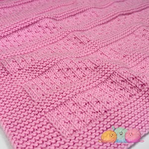 May include: A close-up of a pink knitted fabric with a textured pattern. The fabric is soft and has a subtle sheen.