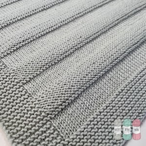May include: A close-up of a light grey knitted fabric with a ribbed texture. The fabric is made with a simple stitch pattern, creating a subtle visual interest.