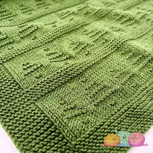 May include: A close-up of a green knitted blanket with a textured pattern. The blanket is made of soft yarn and has a smooth, even texture.