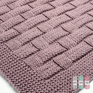 Peut inclure: Gros plan sur une couverture tricotée tissée rose poussiéreux. La couverture présente un motif de tissage en panier, avec des bandes horizontales et verticales de mailles tricotées. La texture est douce et accueillante, idéale pour la décoration intérieure.