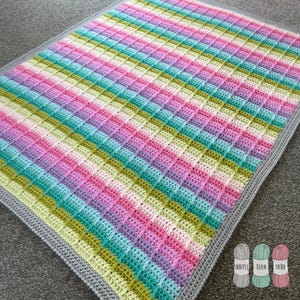 Puede incluir: Una manta de bebé de crochet a rayas de colores con un borde gris. La manta está hecha con una variedad de colores, incluyendo rosa, morado, verde y azul.