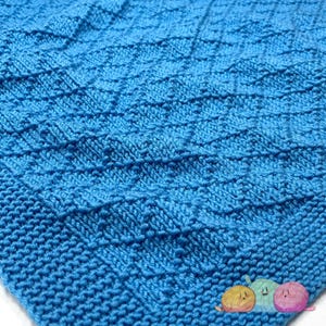 May include: A close-up of a blue knitted blanket with a textured pattern. The blanket is made of soft yarn and has a smooth, even texture.