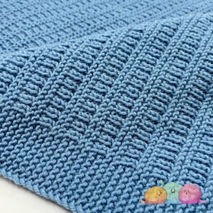 May include: A close-up of a light blue knitted blanket. The blanket has a textured pattern with vertical and horizontal lines, creating a woven appearance. The soft, cozy material is folded over, showing the intricate stitch work.