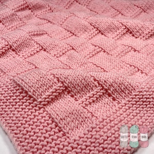 May include: Pink knitted baby blanket with a waffle stitch pattern. The blanket is made with soft yarn and is perfect for cuddling.