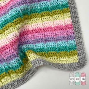 May include: A rainbow striped crochet baby blanket with a grey border. The blanket is folded in half and the yarn balls are visible in the bottom right corner.