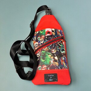 May include: Red crossbody bag with a black adjustable strap. The bag features a colorful print of characters from the Nightmare Before Christmas movie. The bag has a zipper closure and a small patch with the text "SewFine by Lori".