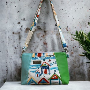 May include: A turquoise, green, and white crossbody bag with a colorful beach hut print. The bag has a zipper closure and a long adjustable strap. The bag is made of fabric and has a leather-like trim. The bag has the text "SeaFine" and "Beach" on it.