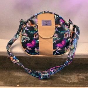 May include: A round black crossbody bag with a butterfly print. The bag has a tan flap with a purple label that says "Seafine by Lori".
