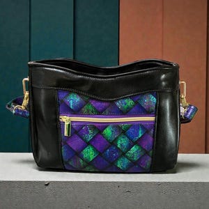May include: Black shoulder bag with a geometric pattern in shades of purple and green. The bag has a gold zipper and hardware, and a black leather exterior. The strap is patterned with purple and blue.