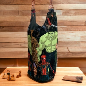 May include: A black canvas tote bag with a colorful print of superheroes, including Hulk and Spiderman. The bag has a brown leather strap and a copper chain.