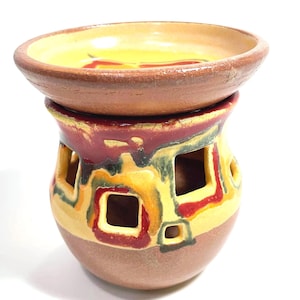 Peut inclure: Un brûle-parfum en céramique composé d'une base arrondie avec des ouvertures carrées et d'une coupelle large et peu profonde sur le dessus. L'objet présente un émail aux tons jaune, rouge et vert foncé sur une argile couleur terre cuite naturelle.