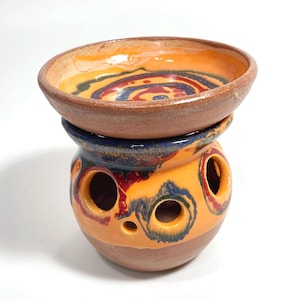 Pode incluir: Um queimador de incenso de cerâmica com um design de redemoinho amarelo, laranja, vermelho e azul. O queimador tem um pequeno prato no topo e furos ao redor dos lados.
