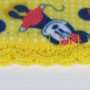 Pu&ograve; includere: Coperta in pile giallo con un motivo a pois bianchi e un'immagine ripetuta di Topolino. La coperta ha un bordo all'uncinetto giallo.