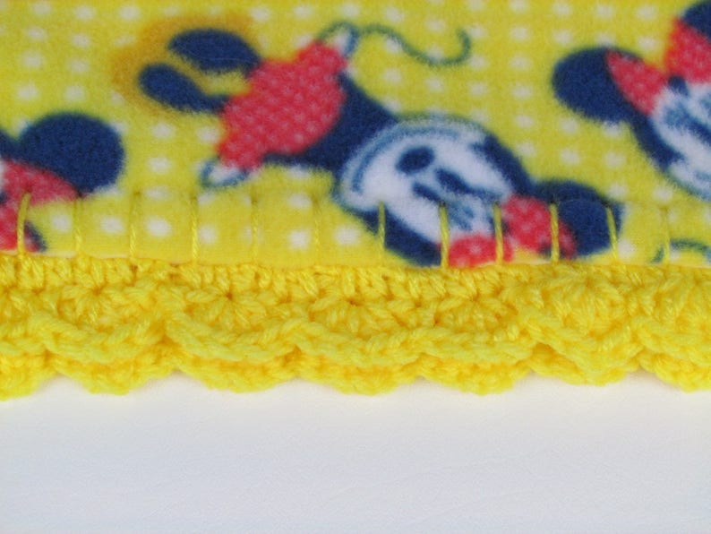 Pu&ograve; includere: Coperta in pile giallo con un motivo a pois bianchi e un'immagine ripetuta di Topolino. La coperta ha un bordo all'uncinetto giallo.