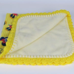Pu&ograve; includere: Coperta per neonati gialla con bordo all'uncinetto e stampa di Topolino su un lato.