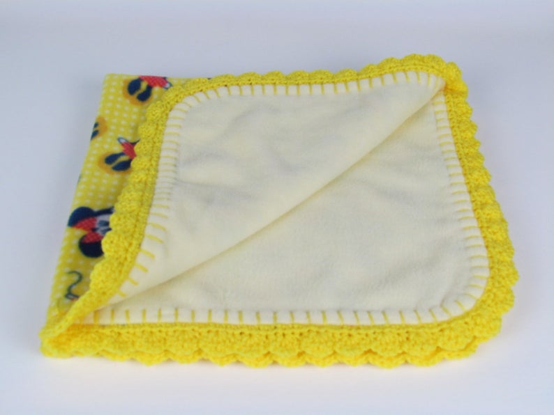 Pu&ograve; includere: Coperta per neonati gialla con bordo all'uncinetto e stampa di Topolino su un lato.