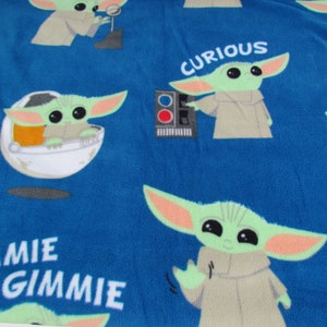 May include: Blue fabric with a repeating pattern of a green alien character with large eyes. The alien is wearing a brown robe and is in different poses. The fabric also has the words "Curious", "Gimme", and "Gimme" printed on it.