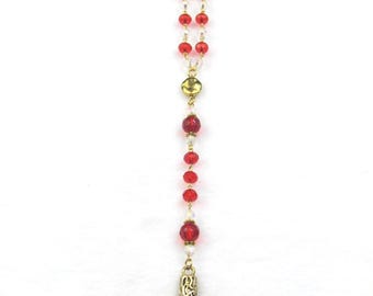 May include: A hanging rosary featuring a series of alternating translucent red and clear faceted beads strung on a gold-toned chain. The rosary terminates in a textured, antique gold-toned metal cross with an intricate, woven-like surface pattern.