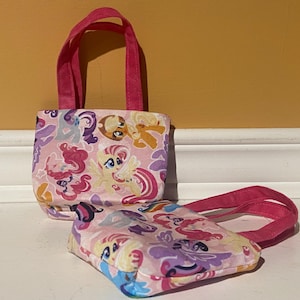 May include: Two small pink tote bags with matching handles. The bags feature a colourful pattern of cartoon ponies in various poses. One bag is upright, and the other is lying down.