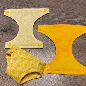 May include: Three yellow cloth diaper inserts. One is plain yellow, another has a white floral design, and the third has a honeycomb pattern. Each has yellow snap fastenings.