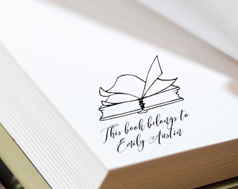 May include: A black and white illustration of an open book with the text "This book belongs to Emily Austin" printed below.