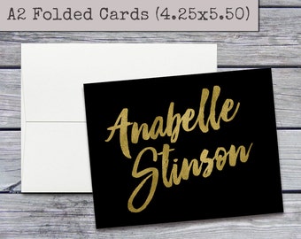 May include: A black card with gold foil lettering that reads "Anabelle Stinson". The card is 4.25 inches by 5.50 inches.