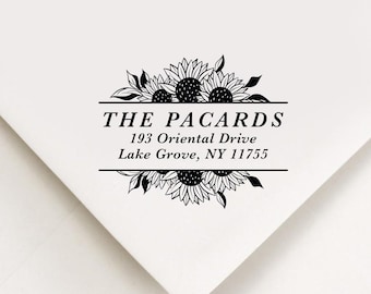 May include: A white envelope corner with a black sunflower design and text. The text reads "THE PACARDS" above the address "193 Oriental Drive Lake Grove, NY 11755". The design includes sunflowers and leaves.