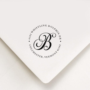 May include: A black and white round return address stamp with the text "6182 Whistling Dolphin Dr. Colchester, Vermont 01192" and a stylized letter "B" in the center.