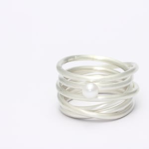 May include: A silver ring with multiple bands wrapped around each other, featuring a single white pearl in the centre.