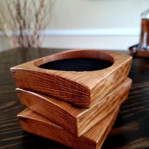 May include: Three wooden coasters stacked on top of each other. The coasters are made of light brown wood with a dark brown stain. The top coaster has a black felt lining.