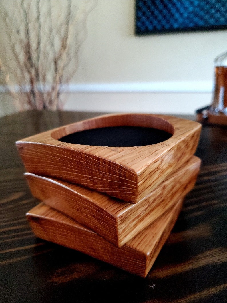 May include: Three wooden coasters stacked on top of each other. The coasters are made of light brown wood with a dark brown stain. The top coaster has a black felt lining.