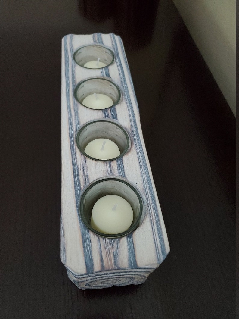 May include: A wooden candle holder with four glass candle holders. The candle holder is painted in shades of gray and white with a wood grain pattern.