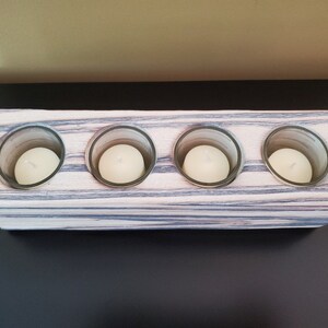 May include: A wooden candle holder with four glass candle holders. The wood is a light brown with dark grey streaks. The candle holders are empty.