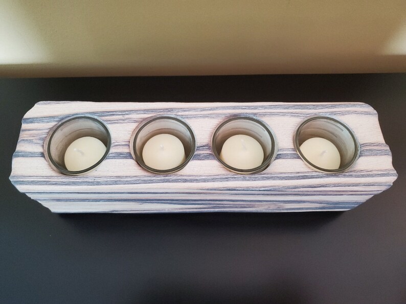 May include: A wooden candle holder with four glass candle holders. The wood is a light brown with dark grey streaks. The candle holders are empty.