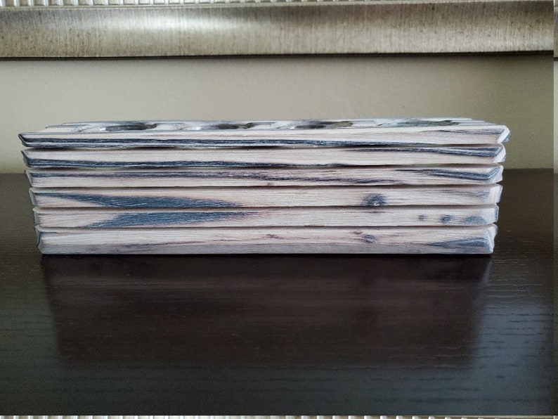 May include: A wooden box with a stacked design, featuring a light brown and black wood grain pattern. The box is made of multiple layers of wood, creating a unique and rustic look.