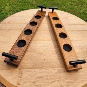 May include: Two wooden beer bottle holders with black metal handles. Each holder has five slots for bottles and a dark brown stain.
