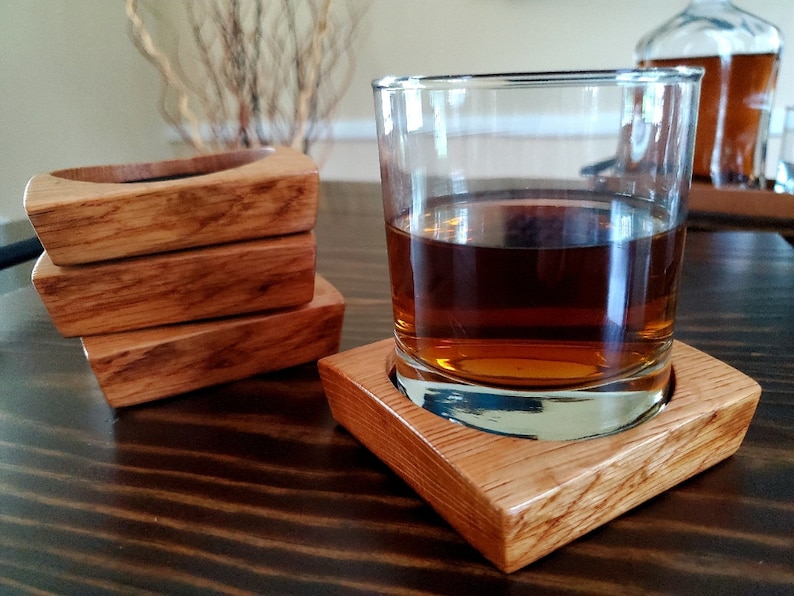 May include: Four wooden coasters stacked on a wooden table with a glass of amber liquid on the top coaster.