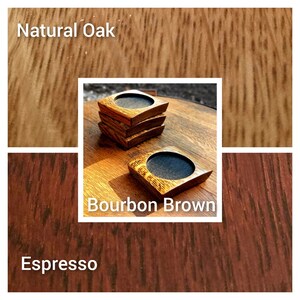 May include: Four wooden coasters in three different shades of brown: natural oak, bourbon brown, and espresso. The coasters are square with rounded edges and have a small circular indentation in the centre.