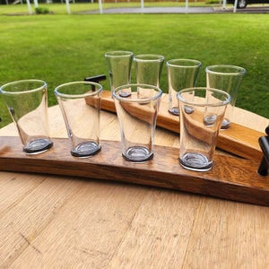 May include: A wooden serving tray with six clear glass shot glasses. The tray is made from reclaimed wood and has two black metal handles. The tray is ideal for serving drinks or snacks.