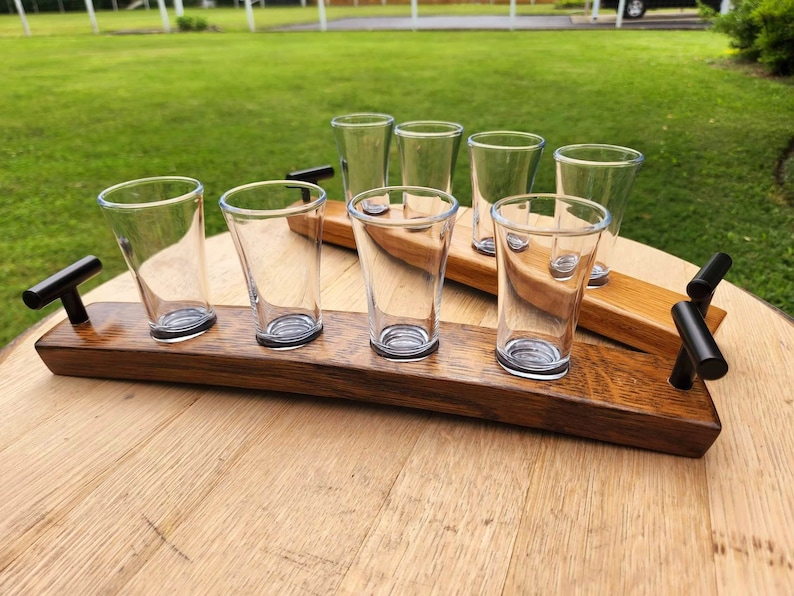 May include: A wooden serving tray with six clear glass shot glasses. The tray is made from reclaimed wood and has two black metal handles. The tray is ideal for serving drinks or snacks.