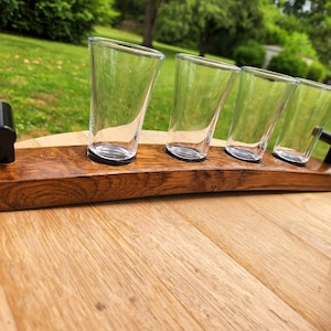 May include: A wooden serving tray with four clear glass shot glasses. The tray is made from reclaimed oak barrel staves and has black metal handles.