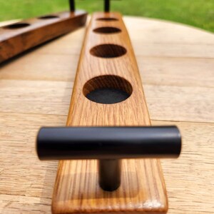 May include: Wooden serving tray with four round cutouts and black handles. The tray is made of light brown wood and has a natural finish.