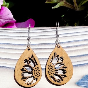 May include: A pair of wooden earrings featuring a sunflower design. The earrings are teardrop shaped and have silver hooks.