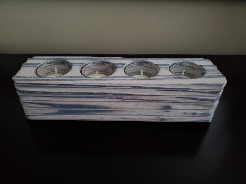 May include: A wooden candle holder with four individual slots for tealight candles. The holder is made of light-colored wood with dark grey streaks throughout.